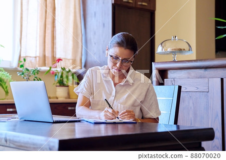 Home workplace, middle aged woman in headphones working using laptop Home workplace, middle aged woman in headphones working using laptop 88070020