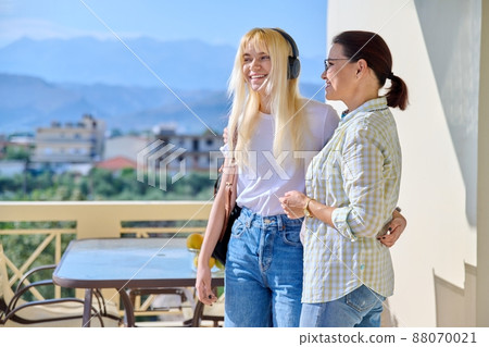 Middle-aged mother hugging her teenage daughter on the porch of the house. 88070021