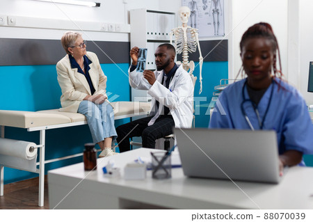 Specialist therapist doctor showing lungs radiography to old woman patient explaining sickness diagnosis discussing healthcare treatment. Medical appointment in hospital office. Medicine concept 88070039