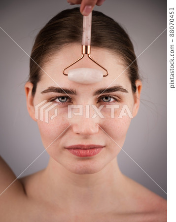 Close-up portrait of a woman uses a quartz roller massager to smooth wrinkles on her forehead. Close-up portrait of a woman uses a quartz roller massager to smooth wrinkles on her forehead. 88070451
