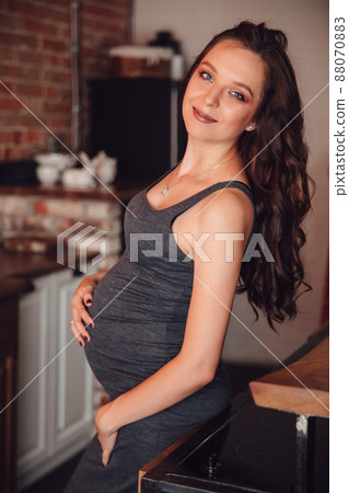a beautiful pregnant woman in a gray dress in the kitchen in the loft style. 88070883