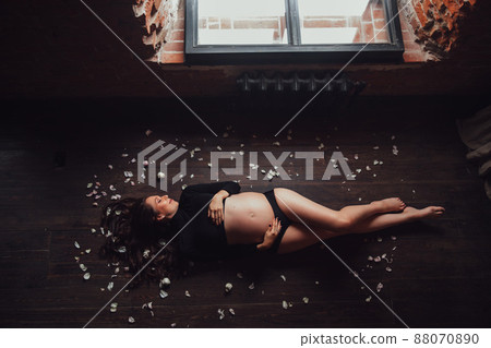 pregnant woman in black with naked belly on floor in petals of white roses 88070890