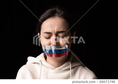 Half-legth portrait of young emotional upset girl with three colors duct tape over her mouth isolated on dark background. Censorship, freedom of speech concept. Half-legth portrait of young emotional upset girl with three colors duct tape over her mouth isolated on dark background. Censorship, freedom of speech concept. 88071746