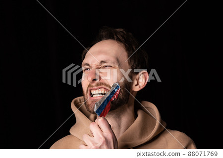 Close-up portrait of young emotive man rips three colors duct tape off his mouth isolated on dark background. Censorship, freedom of speech concept. Close-up portrait of young emotive man rips three colors duct tape off his mouth isolated on dark background. Censorship, freedom of speech concept. 88071769