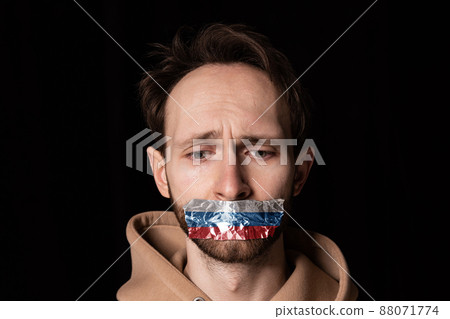 Close-up portrait of young emotive man with three colors duct tape over his mouth isolated on dark background. Censorship, freedom of speech concept. Close-up portrait of young emotive man with three colors duct tape over his mouth isolated on dark background. Censorship, freedom of speech concept. 88071774