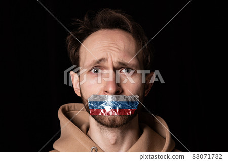 Close-up portrait of young emotive man with three colors duct tape over his mouth isolated on dark background. Censorship, freedom of speech concept. Close-up portrait of young emotive man with three colors duct tape over his mouth isolated on dark background. Censorship, freedom of speech concept. 88071782