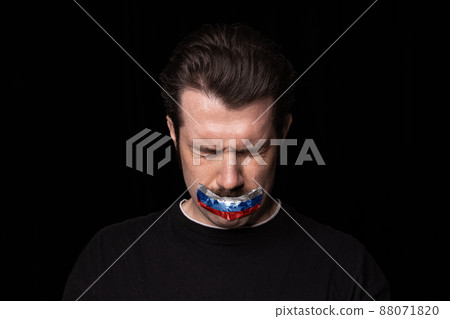 Conceptual portrait of young upset man with three colors duct tape over his mouth isolated on dark background. Censorship, freedom of speech concept. Conceptual portrait of young upset man with three colors duct tape over his mouth isolated on dark background. Censorship, freedom of speech concept. 88071820