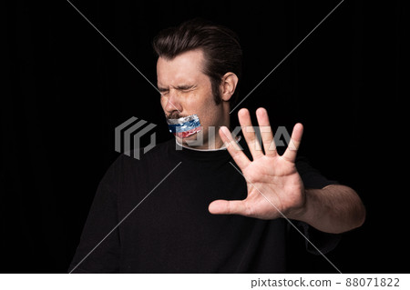 Conceptual portrait of young man with three colors duct tape over his mouth isolated on dark background. Censorship, freedom of speech concept. Conceptual portrait of young man with three colors duct tape over his mouth isolated on dark background. Censorship, freedom of speech concept. 88071822