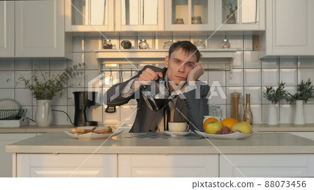 Tired Man Pouring Coffee Early in the Morning, Having Breakfast after Sleepless Night. Coffee Spills over the Rim of Cup. Business, Lifestyle, Overworking Concept 88073456