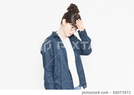 A woman wearing glasses standing in front of a white background and putting her hand on her forehead with fever A woman wearing glasses standing in front of a white background and putting her hand on her forehead with fever 88073972