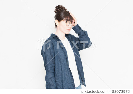A woman wearing glasses standing in front of a white background and putting her hand on her forehead with fever A woman wearing glasses standing in front of a white background and putting her hand on her forehead with fever 88073973