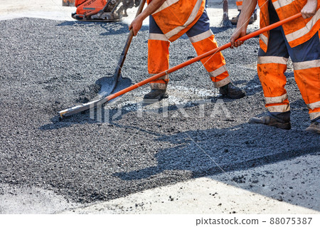 A working team of road builders manually levels the hot asphalt with shovels and metal levels. 88075387