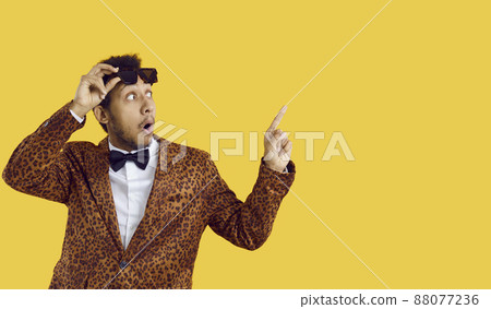 Surprised Afro American man in funky outfit and bowtie takes off his glasses and points index finger to side as he's looking at blank text copyspace studio background with astonished facial expression Surprised Afro American man in funky outfit and bowtie takes off his glasses and points index finger to side as he's looking at blank text copyspace studio background with astonished facial expression 88077236