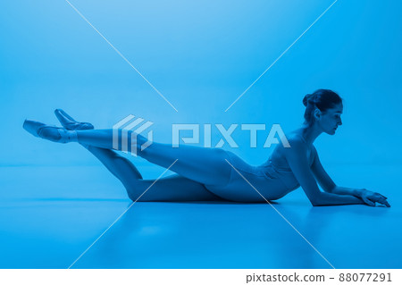 Portrait of beautiful graceful ballet dancer posing isolated on blue studio background in neon light. Art, motion, action, flexibility concept. Portrait of beautiful graceful ballet dancer posing isolated on blue studio background in neon light. Art, motion, action, flexibility concept. 88077291