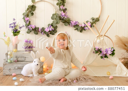 Cute funny baby with bunny ears and colorful Easter eggs at home Cute funny baby with bunny ears and colorful Easter eggs at home 88077451