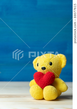 hand make yarn red heart put on yellow teddy bear in front of white pot and green ornamental plants on wooden table and blue background. Concept of valentines day. hand make yarn red heart put on yellow teddy bear in front of white pot and green ornamental plants on wooden table and blue background. Concept of valentines day. 88077615