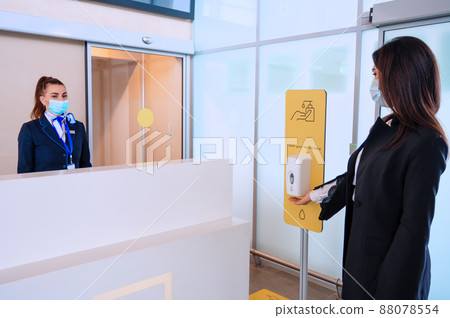Passenger sanitizes hands for check-in in front of airport manager by counter Passenger sanitizes hands for check-in in front of airport manager by counter 88078554