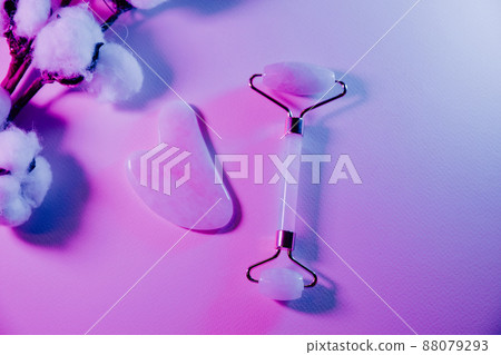 Skin care concept. Jade face roller for beauty facial massage therapy with fern leaf in neon light Skin care concept. Jade face roller for beauty facial massage therapy with fern leaf in neon light 88079293