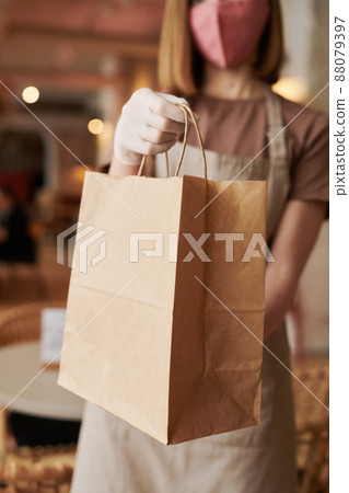 Medium selective focus shot of unrecognizable woman working in cafe wearing mask and gloves giving paper bag with takeaway order to customer Medium selective focus shot of unrecognizable woman working in cafe wearing mask and gloves giving paper bag with takeaway order to customer 88079397