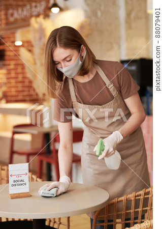 Medium long shot of unrecognizable young waitperson working in modern cafe wiping table with social distance sign on it Medium long shot of unrecognizable young waitperson working in modern cafe wiping table with social distance sign on it 88079401