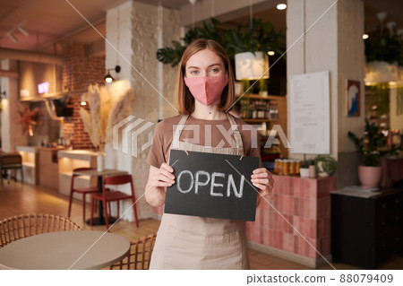 Horizontal medium portrait of unrecognizable woman working in cafe standing indoors holding sign with word Open Horizontal medium portrait of unrecognizable woman working in cafe standing indoors holding sign with word Open 88079409