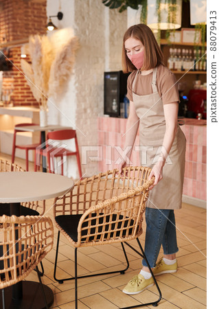 Vertical full shot of modern female waitperson preparing table and chairs for new customers in cozy cafe Vertical full shot of modern female waitperson preparing table and chairs for new customers in cozy cafe 88079413