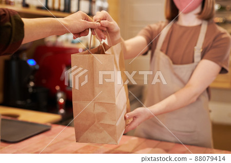 Medium section selective focus shot of unrecognizable female cafe worker standing at counter giving takeaway meal in paper bag to customer 88079414