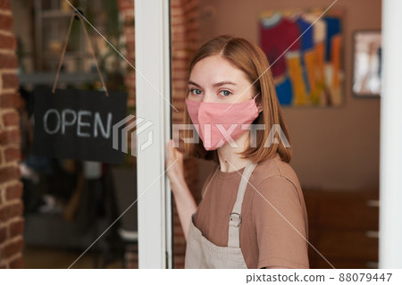 Horizontal medium close-up portrait of young Caucasian woman wearing protective mask on face starting workday with opening cafe Horizontal medium close-up portrait of young Caucasian woman wearing protective mask on face starting workday with opening cafe 88079447