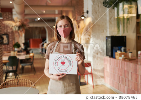 Horizontal medium shot of unrecognizable female waitperson holding Face Mask Required sign looking at camera Horizontal medium shot of unrecognizable female waitperson holding Face Mask Required sign looking at camera 88079463