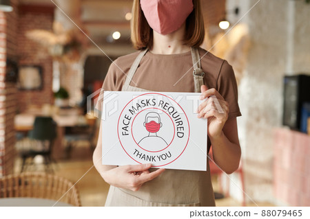 Horizontal shot of unrecognizable cafe worker standing alone holding Face Mask Required sign Horizontal shot of unrecognizable cafe worker standing alone holding Face Mask Required sign 88079465