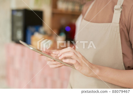 Horizontal medium section close-up shot of unrecognizable woman wearing apron working in cafe using digital tablet Horizontal medium section close-up shot of unrecognizable woman wearing apron working in cafe using digital tablet 88079467