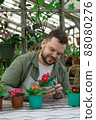 Young farmer inspects pots of flowers before selling and smiles. Gardening, seedlings, sales 88080276