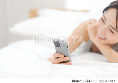 一名婦女在床上的看一個智能手機 一名婦女在床上的看一個智能手機 88080787
