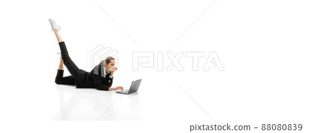 Portrit of young businesswoman in official black suit lying on floor and typing on laptop isolated over white studio background Portrit of young businesswoman in official black suit lying on floor and typing on laptop isolated over white studio background 88080839