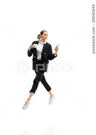 Dynamic portrait of young woman, office worker in black official suit having video call on phone isolated over white studio background 88080848