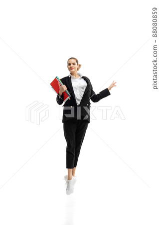 Dynamic portrait of young businesswoman in black suit jumping with folders isolated over white studio background 88080859