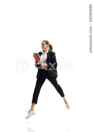Dynamic portrait of young businesswoman in black suit holding folders, in motion isolated over white studio background 88080866