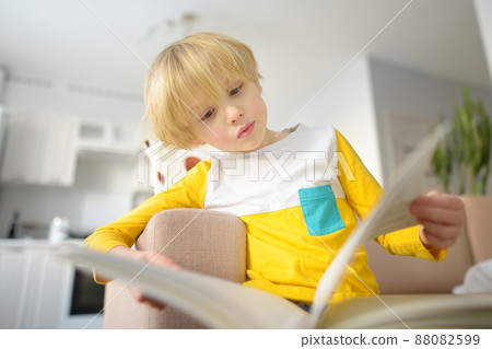 Little boy is reading a book at home. Preschool child is watching at pictures in a book with a fairy tale. A child of primary school age is learning to read. 88082599