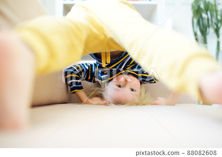 Little boy is standing on own head on sofa at home. Bored lonely child. Difficulties of family with preschool children during working at home. Baby having fun and standing upside down. 88082608