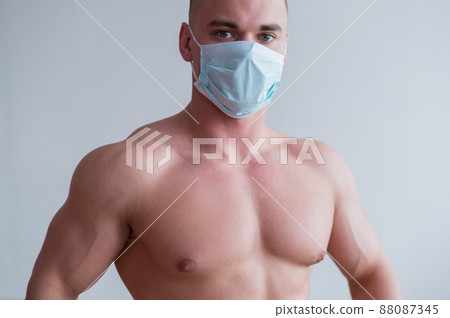 Male bodybuilder in a medical mask with muscular bare chest. The guy goes in for sports in quarantine. Respiratory protection. 88087345