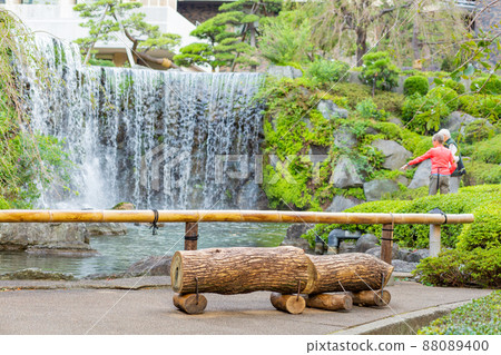 [Japan] Tokyo, a waterfall in a Japanese garden and a log bench placed in front of it 88089400