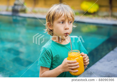Boy drinking juicy smoothie from mango in glass mason jar with steel straw on the background of the pool. Healthy life concept, copy space Boy drinking juicy smoothie from mango in glass mason jar with steel straw on the background of the pool. Healthy life concept, copy space 88090366