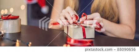 Young woman is packing presents. Present wrapped in craft paper with a red and gold ribbon for christmas or new year. Woman makes an advent calendar for her child BANNER, LONG FORMAT 88090656