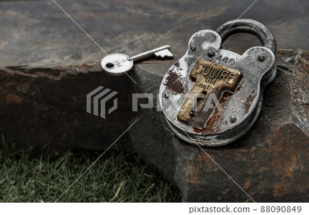 Old vintage iron padlock with key on Huge stone over green grass background. Old vintage iron padlock with key on Huge stone over green grass background. 88090849