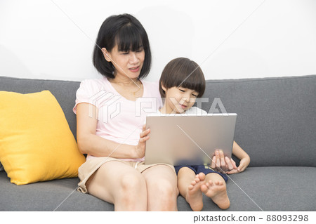 young asian mother and son sitting on sofa using digital tablet happy and smiling. 88093298