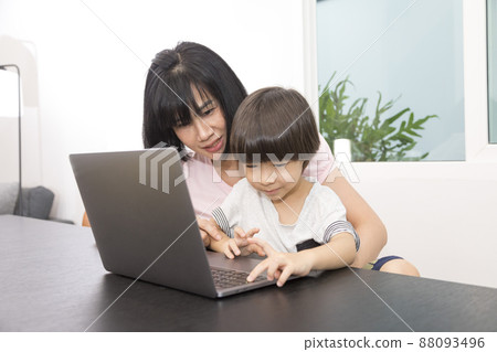 Asian woman with a child works on computer. Concept of work from home and home family education. Mom and son are working on a laptop at home. Asian woman with a child works on computer. Concept of work from home and home family education. Mom and son are working on a laptop at home. 88093496