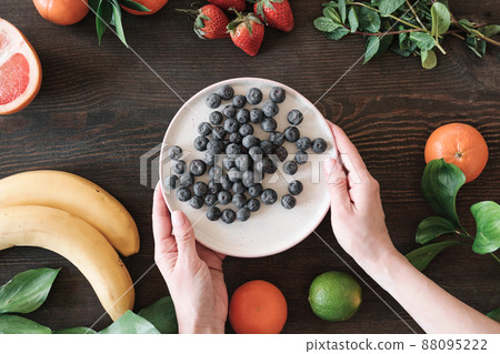 Directly above view of unrecognizable woman putting plate of blueberries on table with fresh ripe fruits 88095222