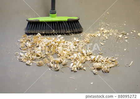 a small pile of wood shavings on a gray linoleum floor with a broom brush 88095272