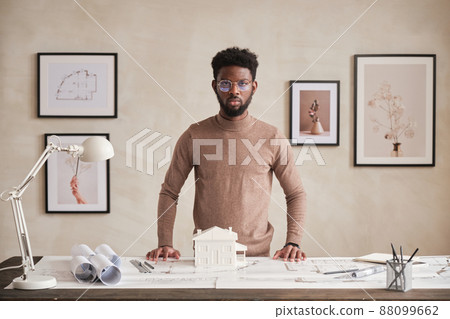 Portrait of serious confident African American architect in round-shaped eyeglasses standing at table with blueprints in office 88099662
