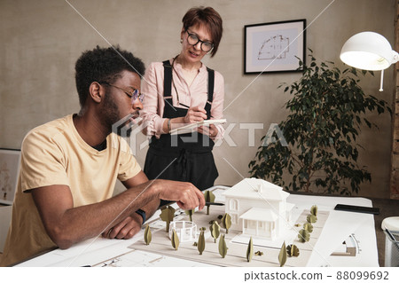 Young African-American architect in glasses pointing at D model and discussing landscape design with colleague 88099692